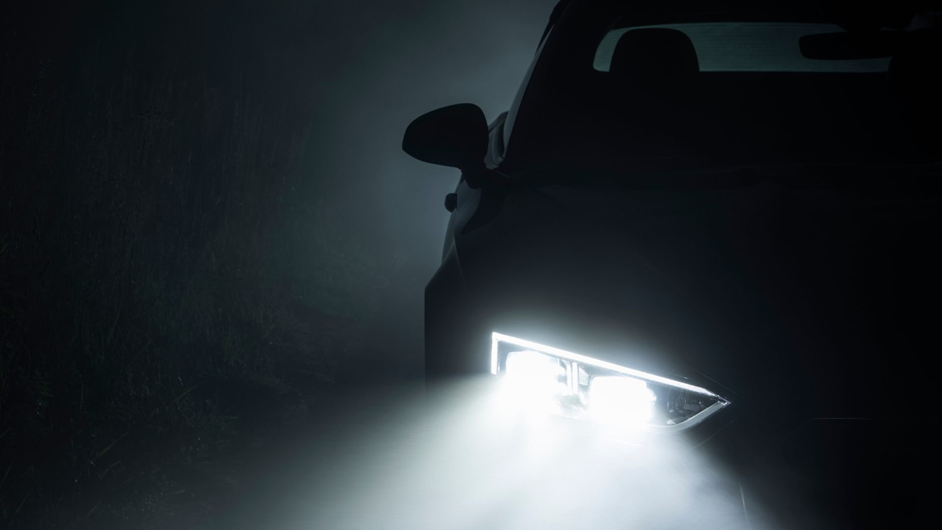 Car headlight glowing brightly in dark, misty environment