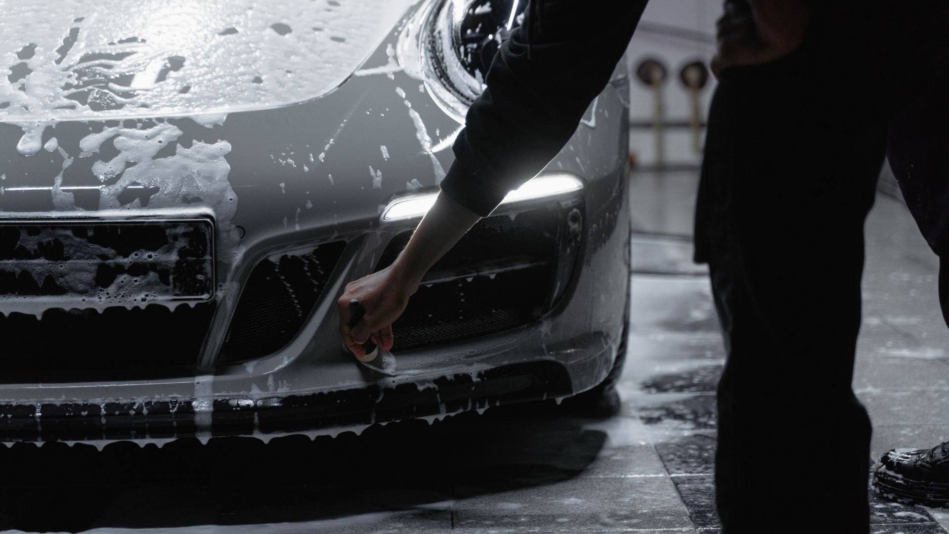 Hand washing car with soapy water in dark, wet car wash