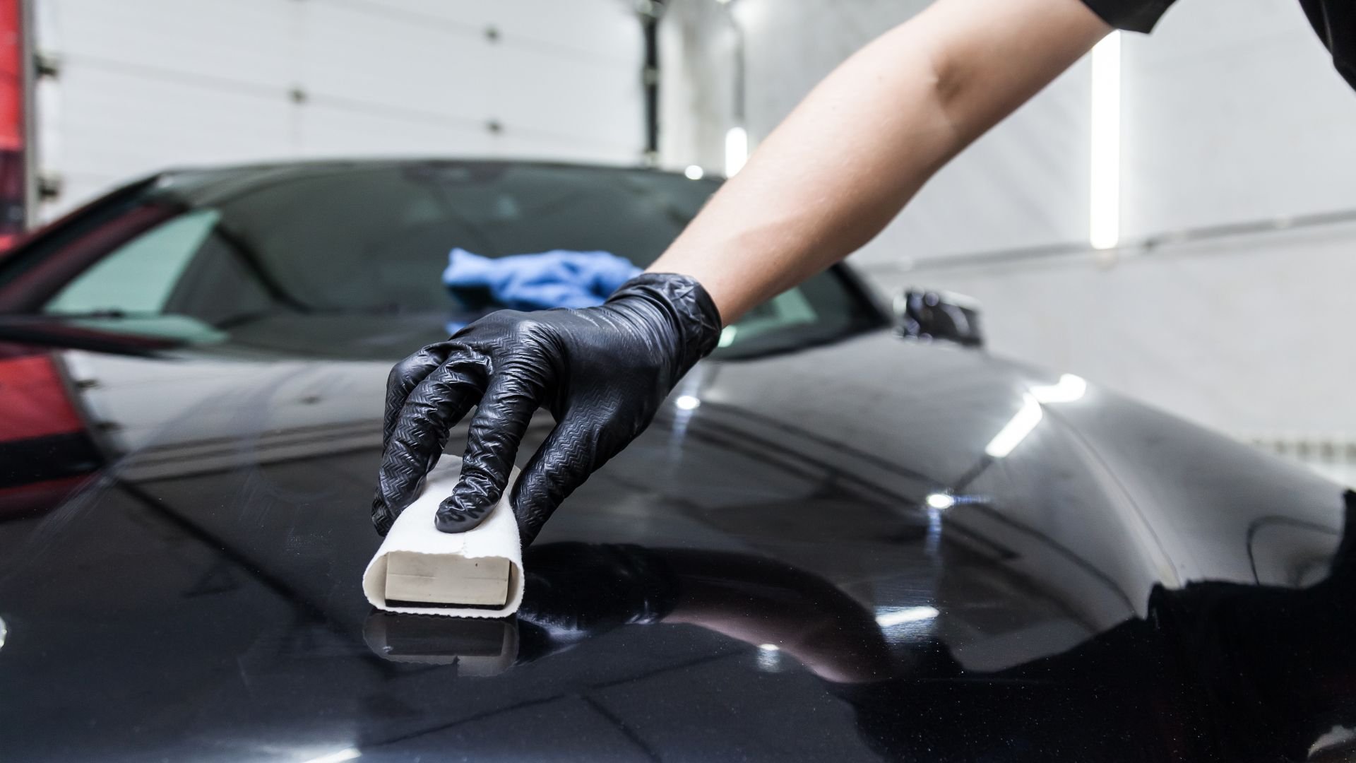 Car detailing with gloved hand polishing sleek black vehicle surface