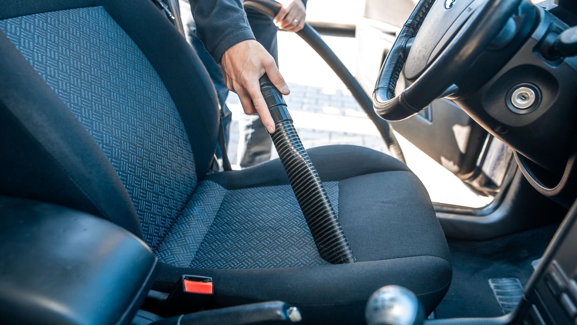 Person vacuuming car interior with handheld vacuum cleaner