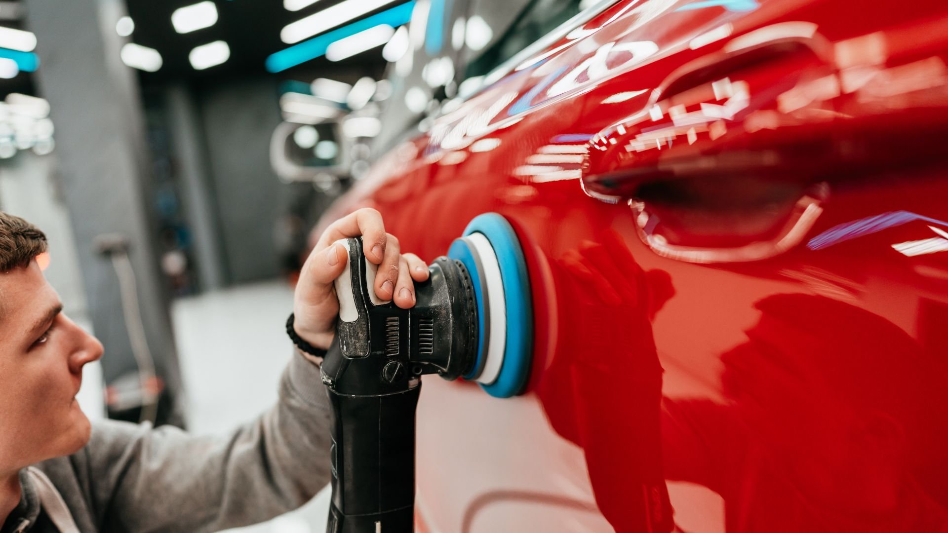 Polishing a red car with an electric buffer in auto detailing shop